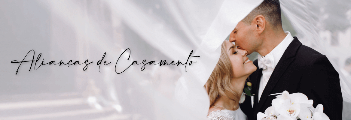 Casal em roupa de casamento envolto num véu branco, dedicado para a categoria alianças de casamento.